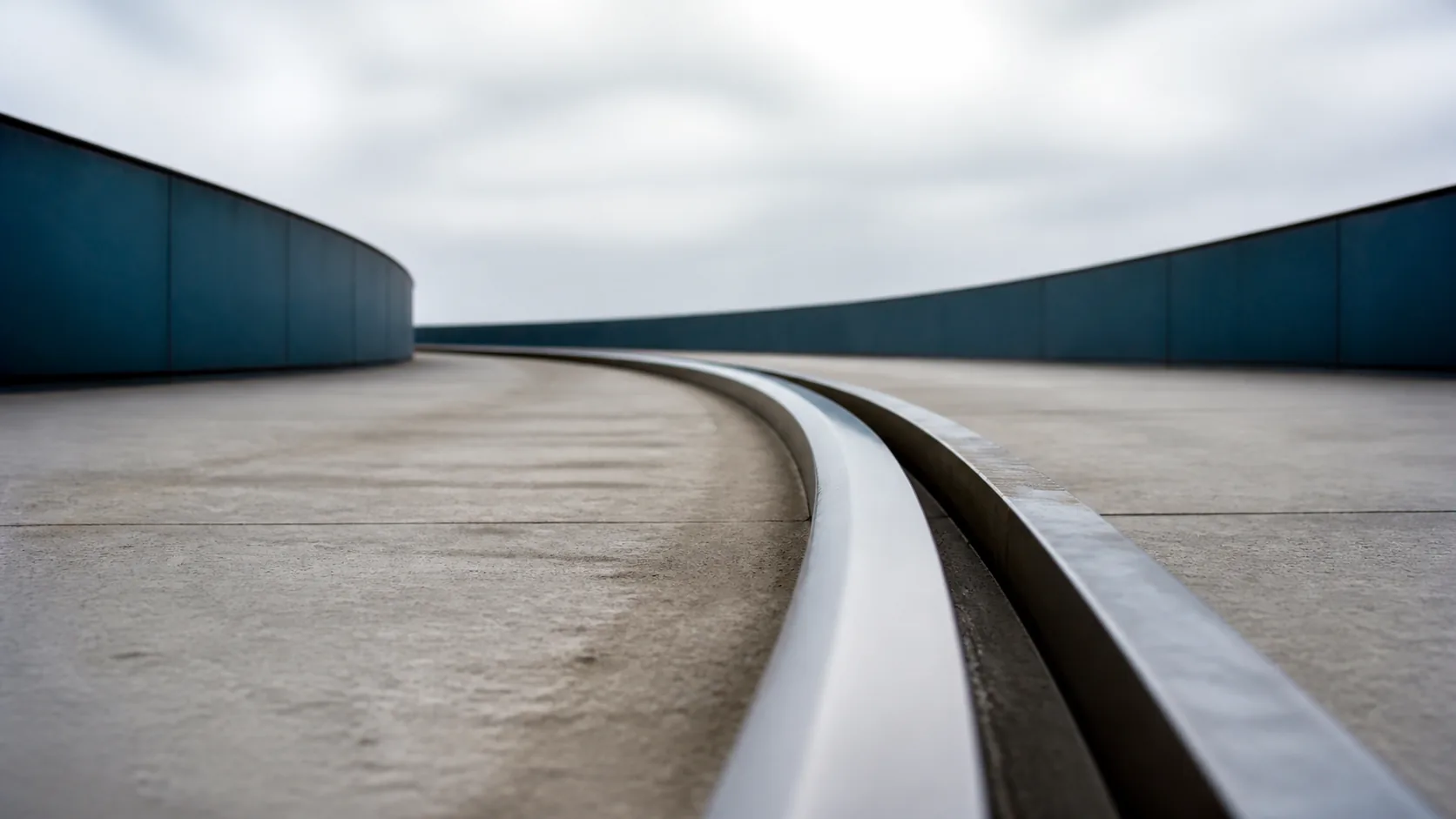 Long curved steel rail on a concrete platform photographed from a low angle so the curve sweeps up on both sides