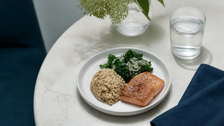 Photoreal editorial overhead still life of a small white ceramic plate holding a modest, carefully portioned meal of grains