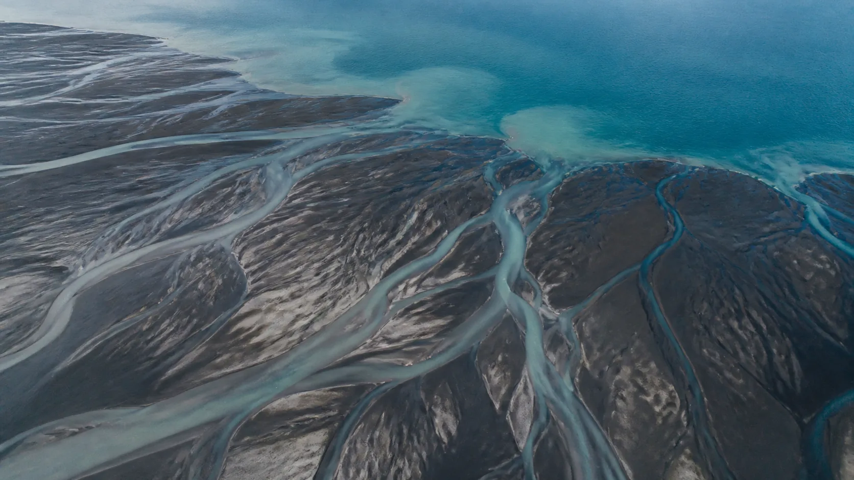 Aerial view of a river delta braiding into many channels through dark silt at low light, some channels silted shut