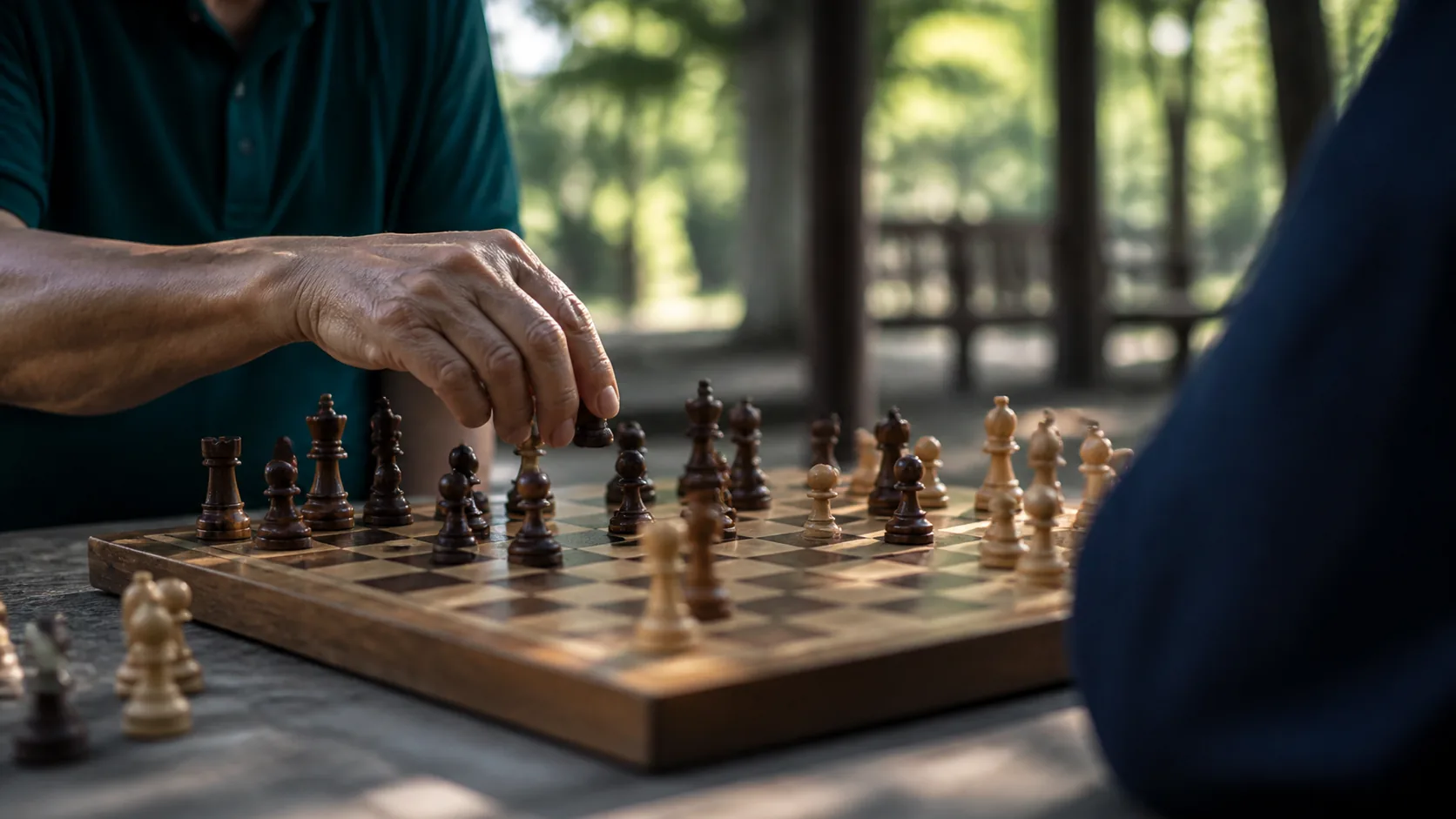 Worn wooden chess board mid-game in a park pavilion, a hand hovering over a piece, dappled afternoon light through leaves