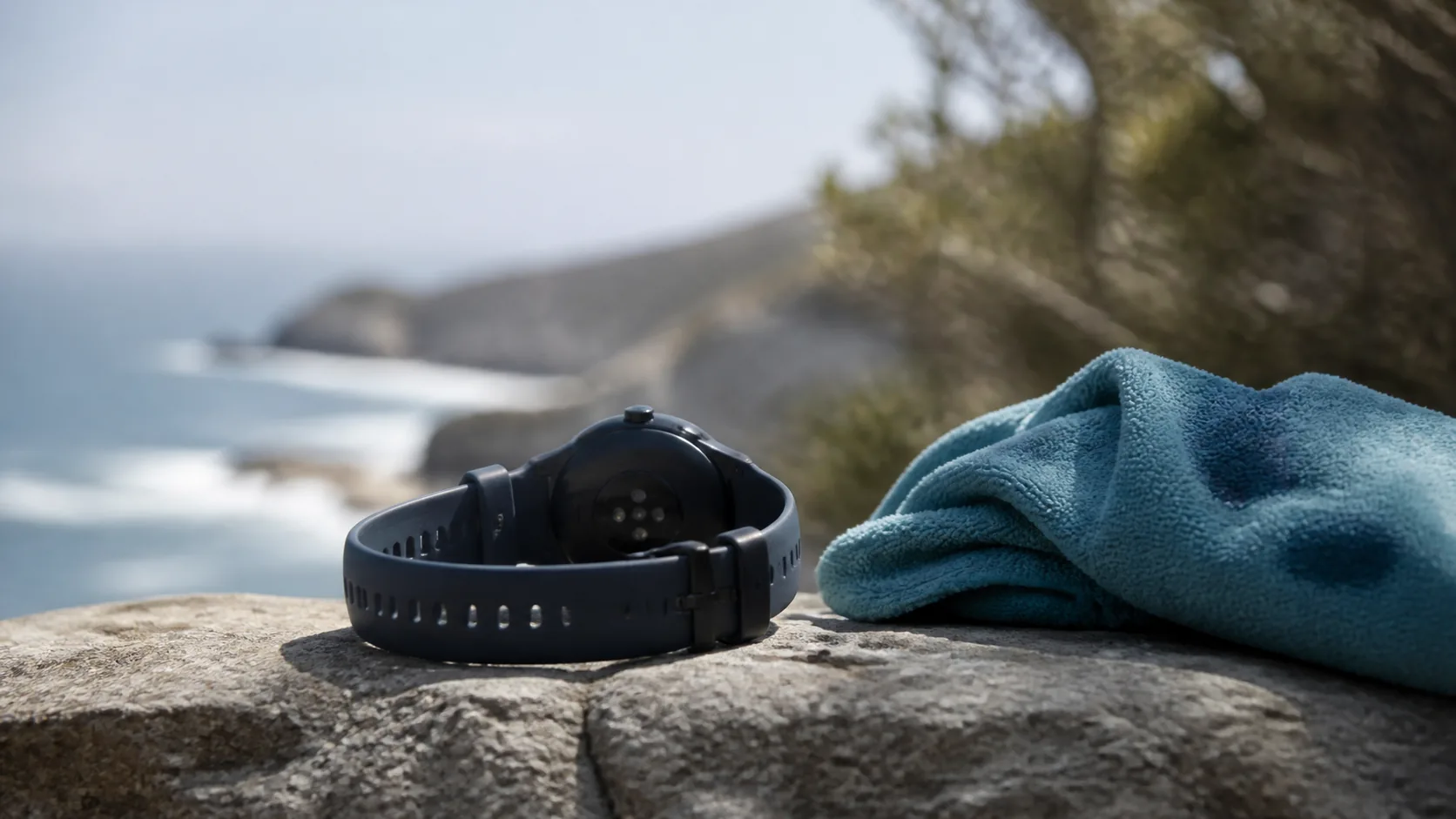 Running watch lying face down on a stone wall beside a folded towel after a run, sweat marks on the fabric
