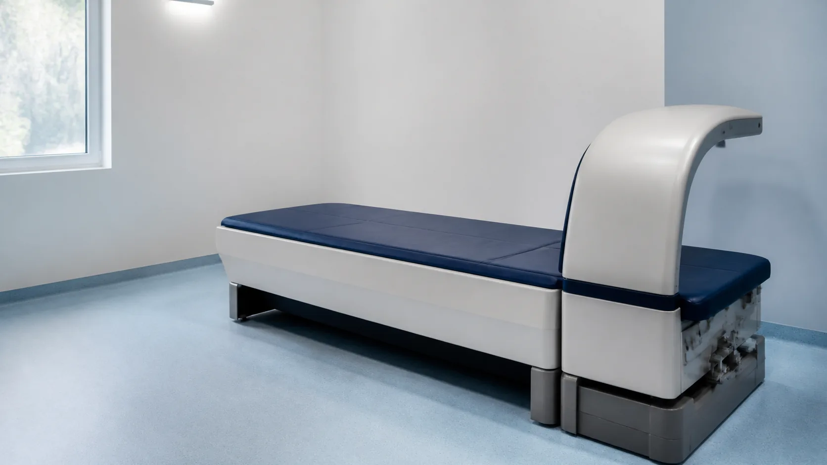 DXA scanning bed with its overhead arm parked at the foot of the table in a bright, empty imaging room
