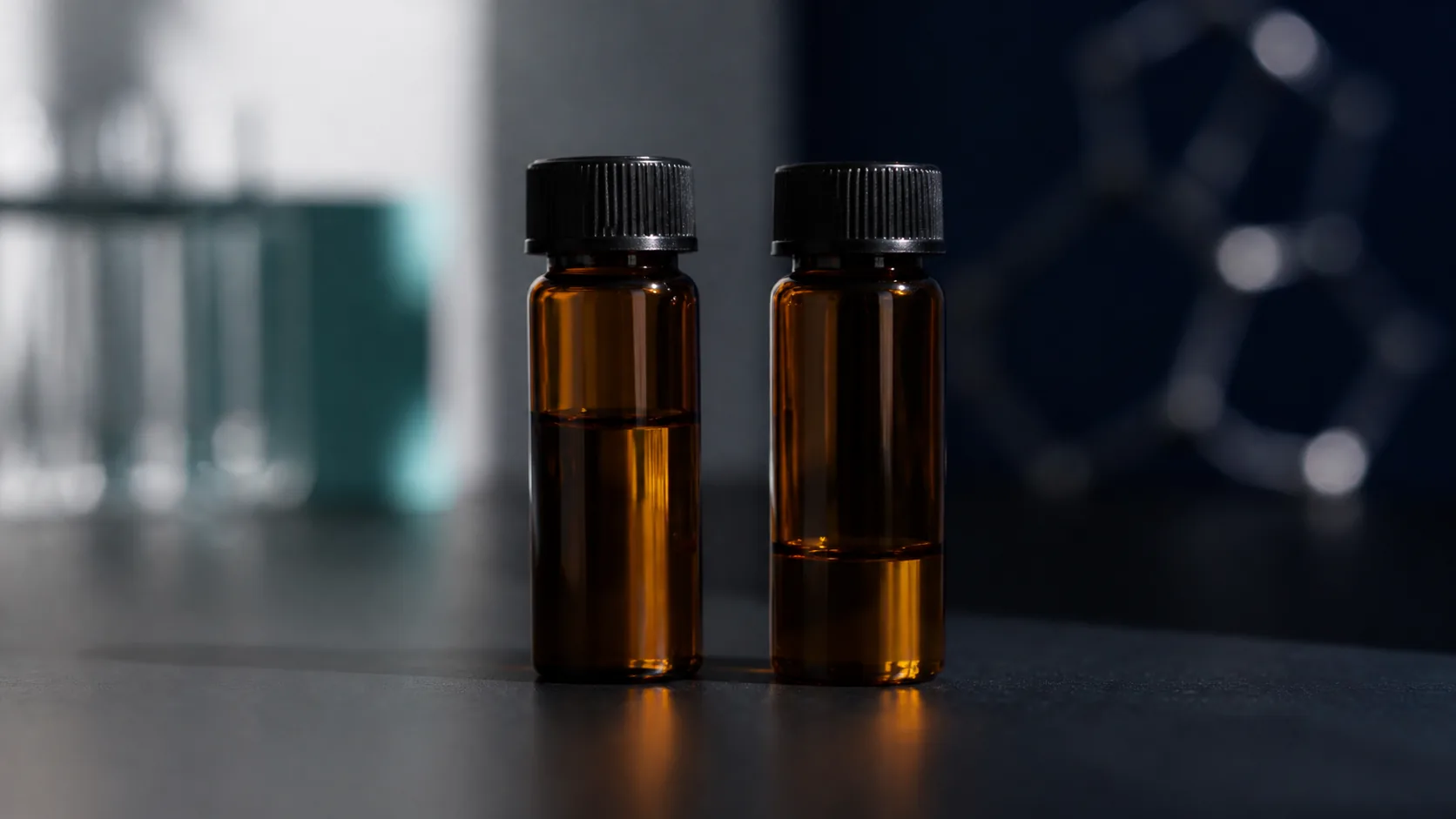 Two amber sample vials of unequal fill standing side by side on a matte black surface