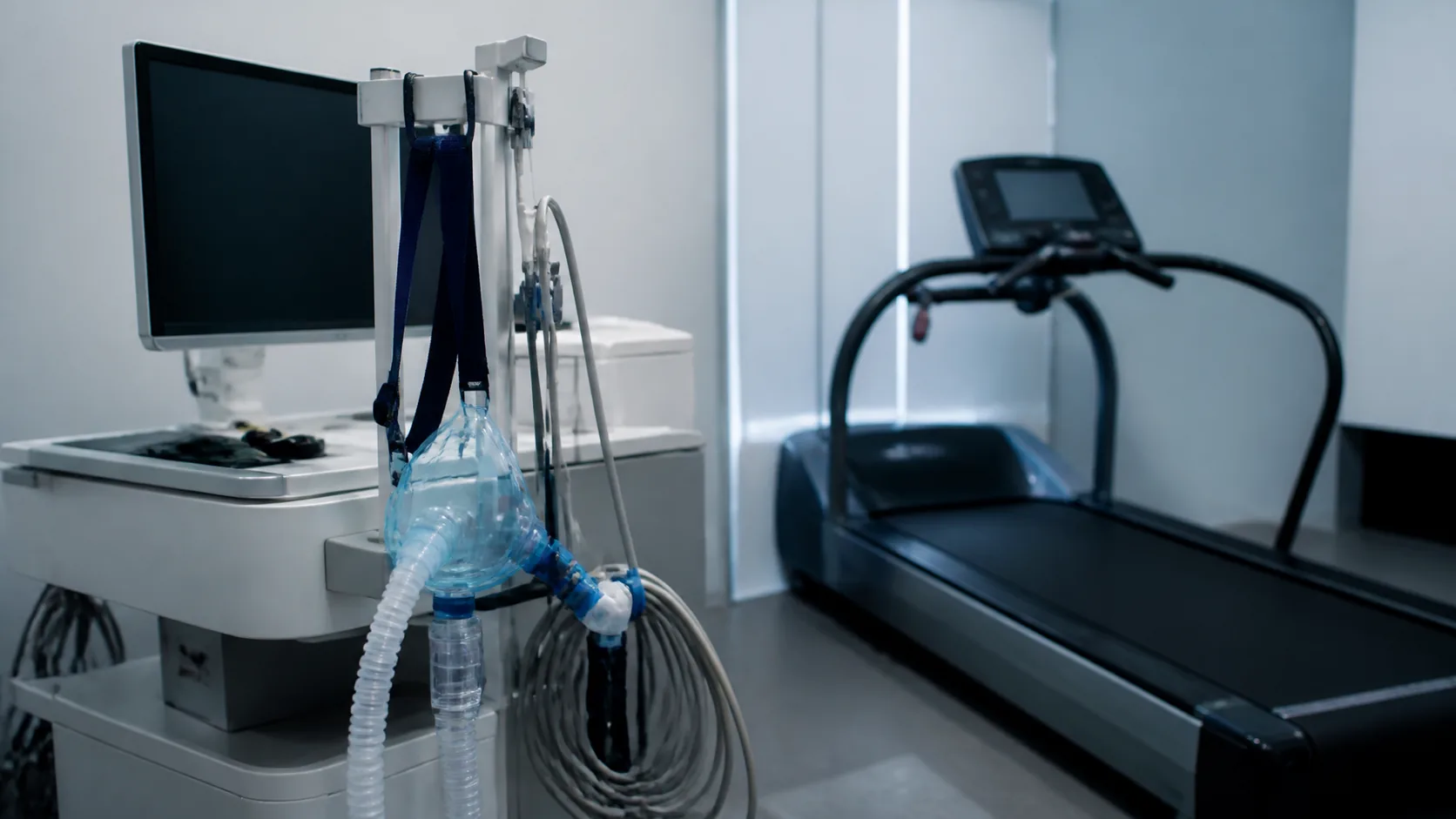 Metabolic cart with its breathing mask and corrugated tube hanging beside a treadmill in an exercise physiology laboratory