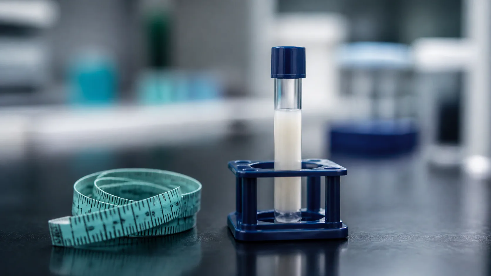 Cloth tape measure beside a single blood tube of cloudy, milky serum standing in a small rack on a dark laboratory bench