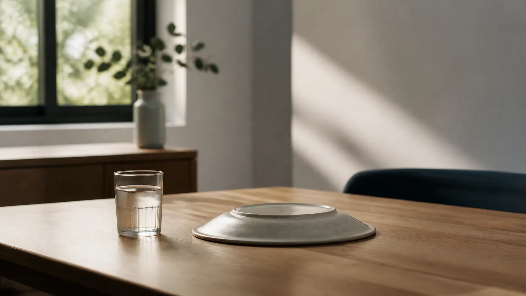 Cleared kitchen table with a single glass of water and an upturned empty plate, morning light through a window