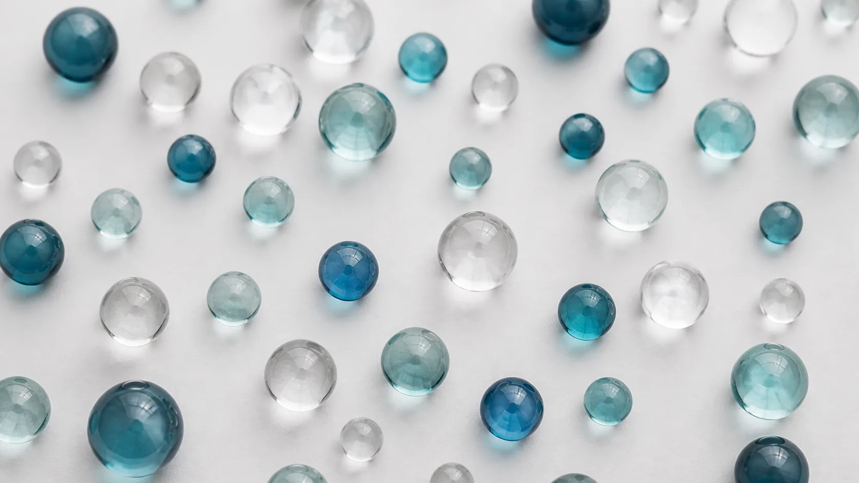 Identical clear glass marbles of slightly different sizes scattered on a matte white surface, top-down macro, soft even light