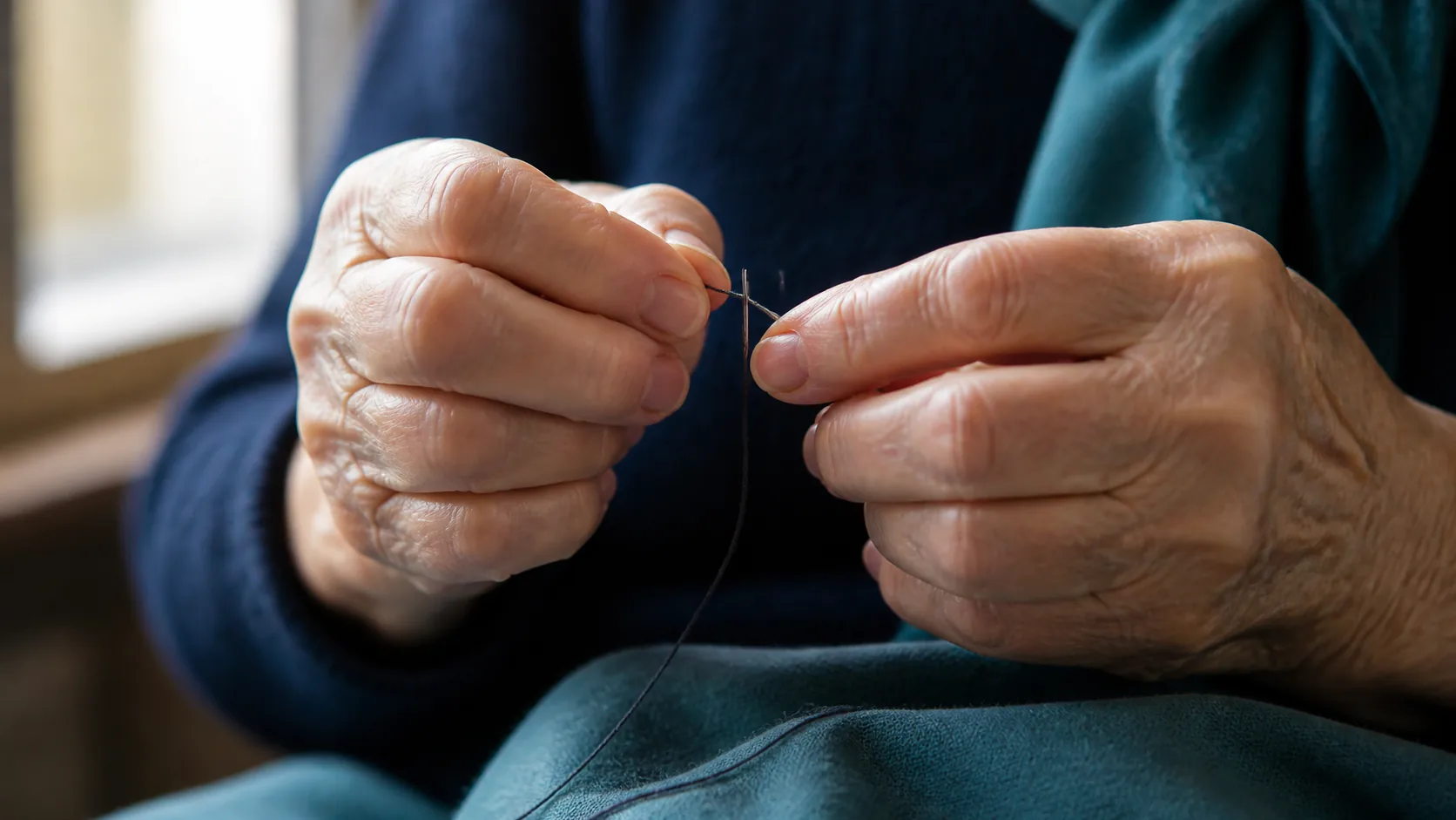 Older person's hands threading a needle in good light, steady and precise, warm window light, close crop on the hands only